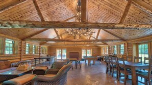 A spacious lodge with a high wooden ceiling, large windows, and a central fireplace.