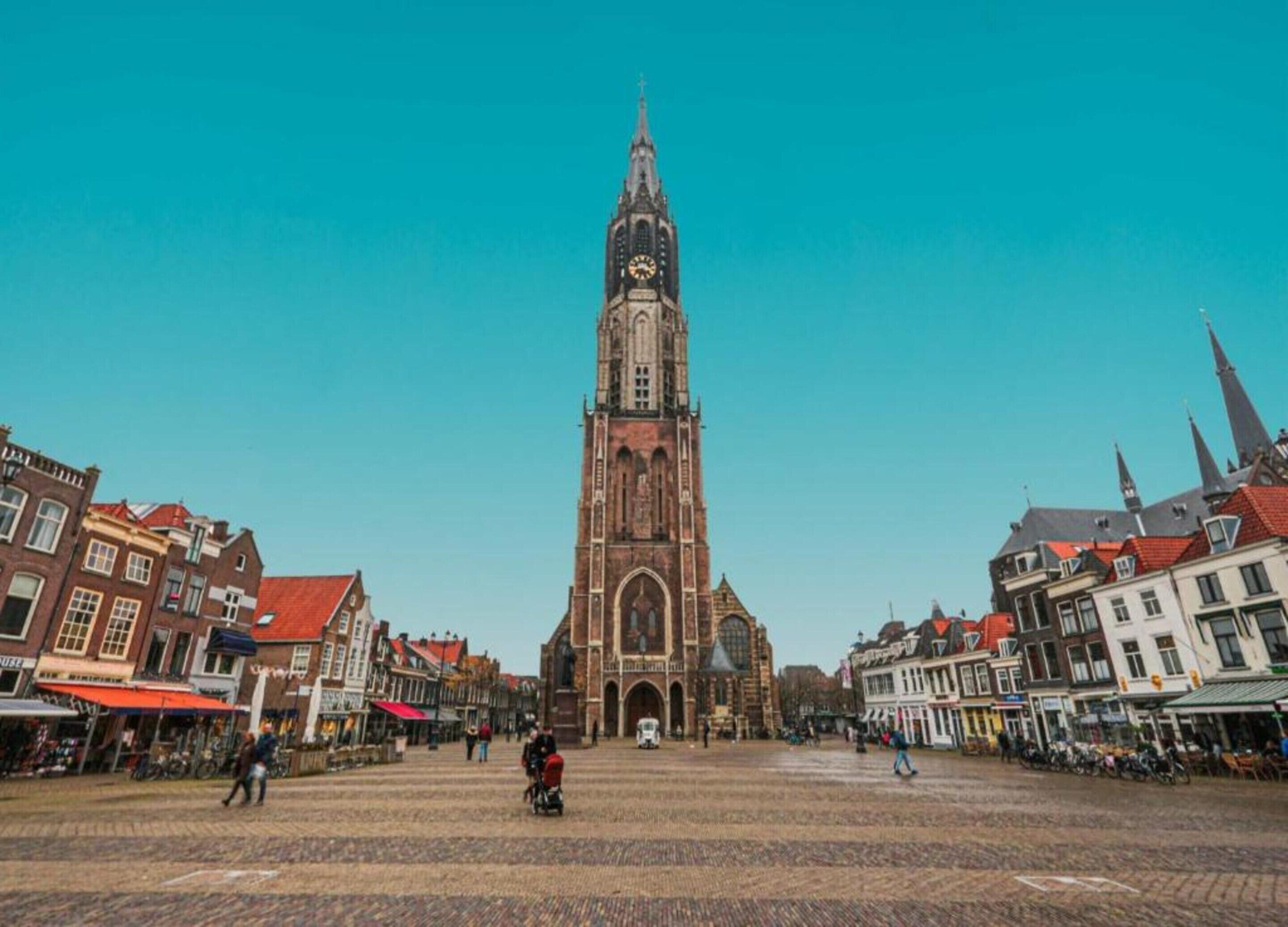 Une place historique, dominée par un imposant clocher d’église, dont le sol est pavé de pierres et qui est bordée de bâtiments à l’architecture traditionnelle.