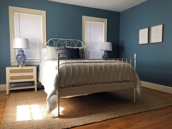 A bedroom with a bed, two nightstands, two lamps, a rug, and two windows with blinds.