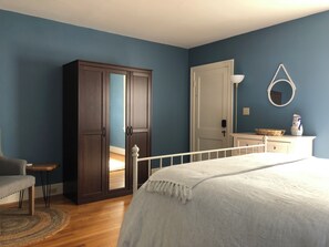 A bedroom with a bed, a wardrobe, a dresser, a mirror, and a door.