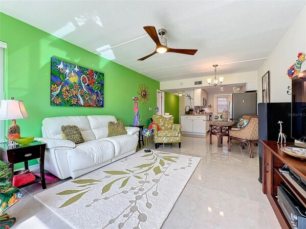 A living room with a white sofa, green walls, a ceiling fan, and a dining area with a table and chairs.