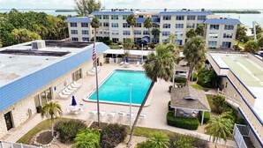 A hotel with a swimming pool surrounded by lounge chairs and palm trees.