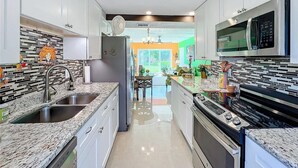 A modern kitchen with white cabinets, granite countertops, a stainless steel refrigerator, and a built-in microwave.