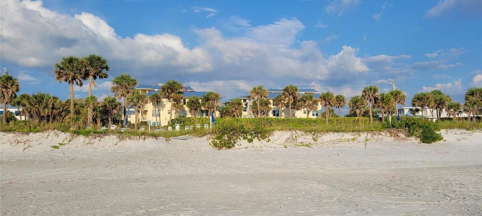 A beachfront hotel with multiple-story buildings, palm trees, and a sandy beach.