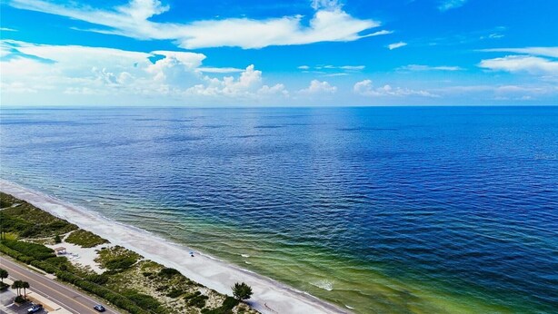 An aerial view of a beach with clear blue waters and a road running parallel to the shore.