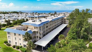 A multi-story hotel with a flat roof, a covered parking area, and a view of the ocean.