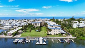 A marina with multiple boats docked, a large building with a blue roof, and a clear view of the ocean.