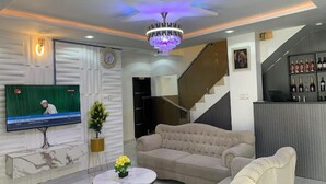 A modern living room with a beige sofa, a marble coffee table, a TV mounted on the wall, and a chandelier. - KD Hotel and Apartment (Ibadan)