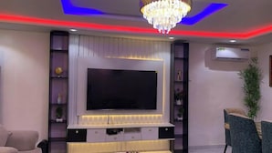 A modern living room with a large flat-screen TV, a chandelier, and a dining area with chairs and a table. - KD Hotel and Apartment (Ibadan)