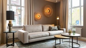 Ein modernes Wohnzimmer mit einem beigefarbenen Sofa, zwei runden Beistelltischen und dekorativen Wandleuchten.