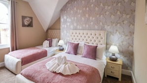 A bedroom with two beds, a large window, and a decorative wall. - Tennyson Grange (Bridlington)