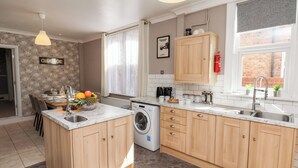 A modern kitchen with wooden cabinets, a built-in washing machine, and a dining area with a table set for two. - Tennyson Grange (Bridlington)