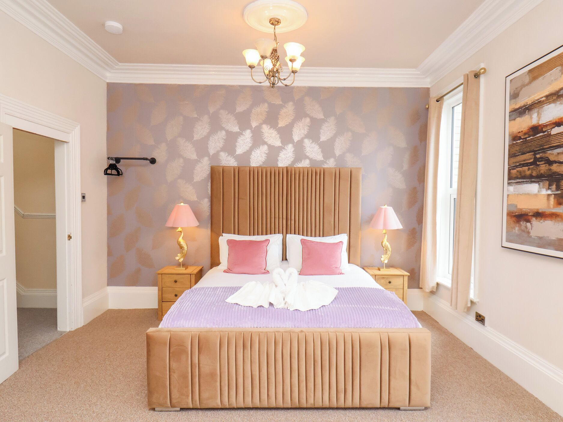 A bedroom with a large bed, two bedside tables with lamps, a chandelier, a door, and a patterned wallpaper.