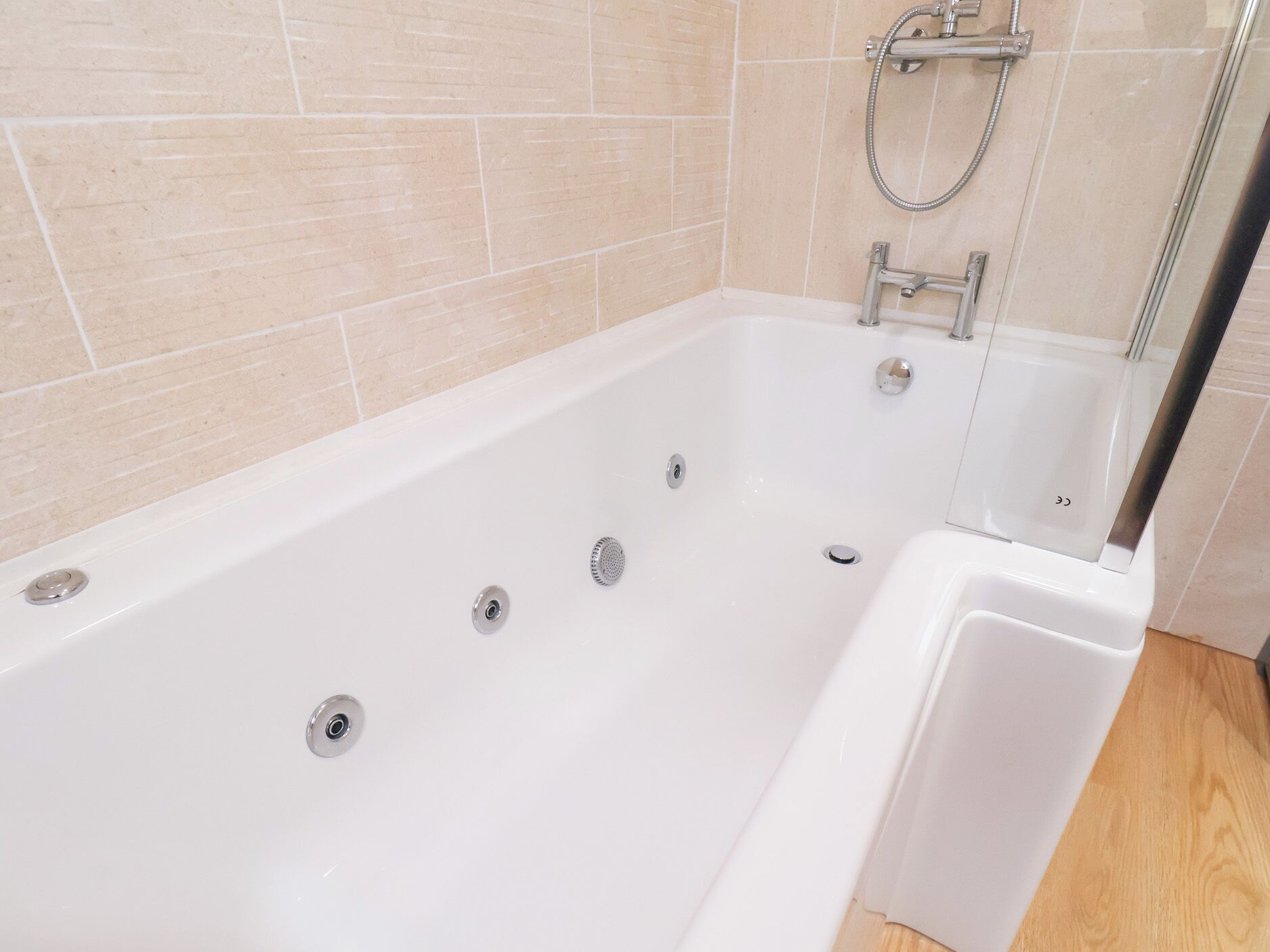 A modern bathroom with a white bathtub, a glass shower enclosure, and beige tiled walls.