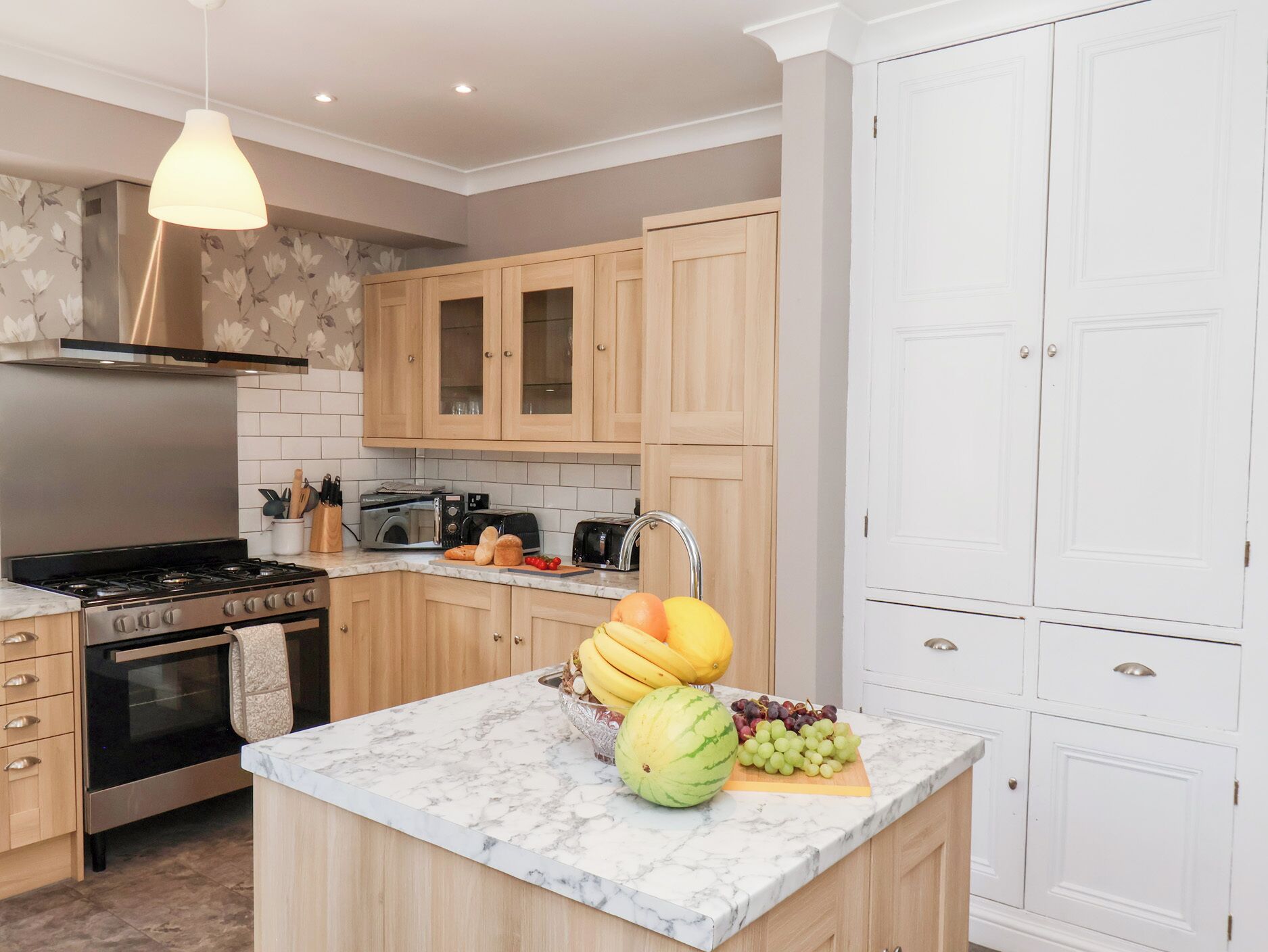 A modern kitchen with wooden cabinets, a marble countertop, a gas stove, a microwave, and a sink.
