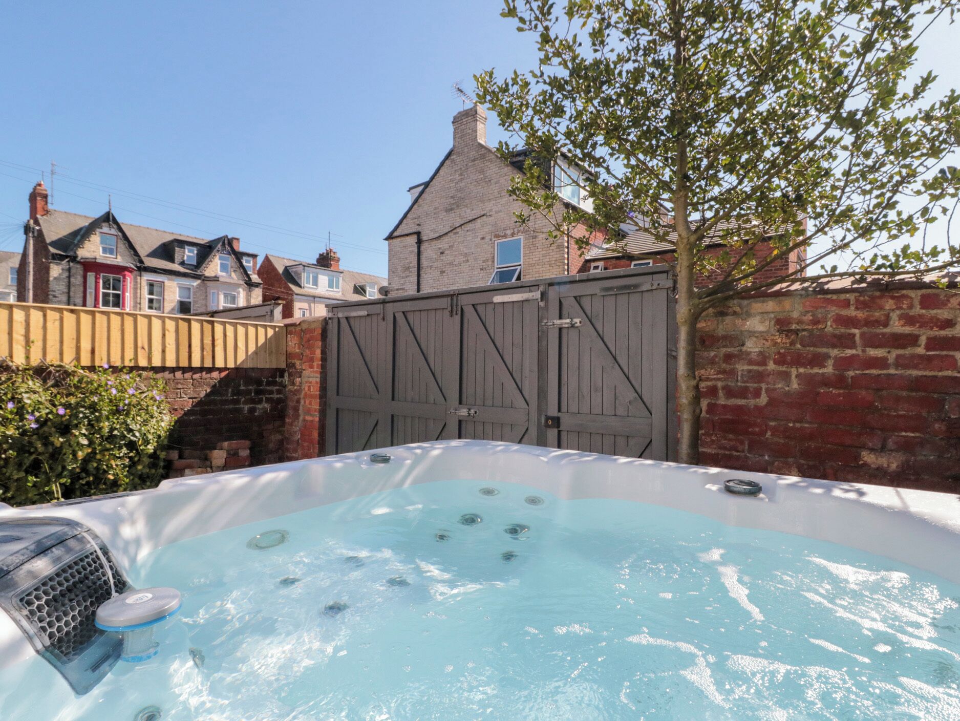 Un jacuzzi en un patio trasero con un muro de ladrillo y una valla de madera.