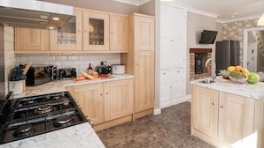 A modern kitchen with wooden cabinets, a gas stove, and a countertop with various appliances and food items. - Tennyson Grange (Bridlington)