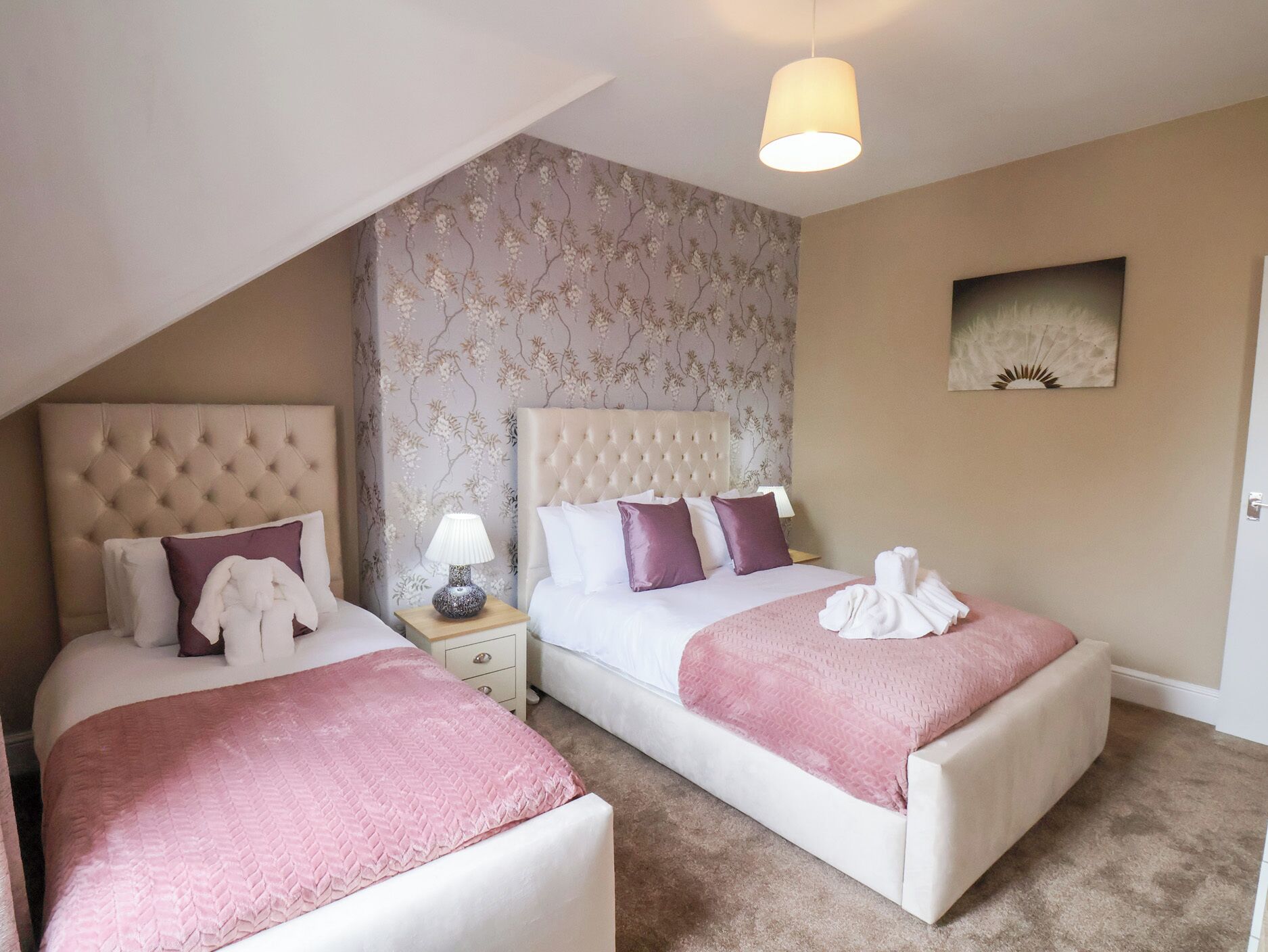 Een hotelkamer met twee bedden, een kroonluchter, bloemenbehang en een schilderij aan de muur.