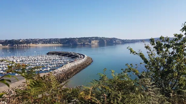 Uma marina com vários barcos atracados, rodeada por terreno rochoso e colinas ao fundo.