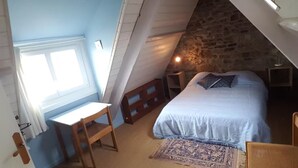 Quarto com cama, escrivaninha, cadeira, tapete e parede de pedra.