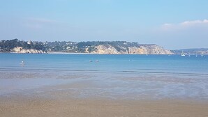 Uma praia com águas cristalinas, areal arenoso e um escarpe rochoso ao fundo.