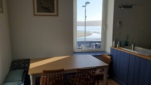 Uma área de refeições com vista para a praia, uma janela com vista para a praia, uma cadeira, uma mesa e um banco.