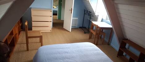 A bedroom with a bed, two wooden chairs, a desk, and a wardrobe.