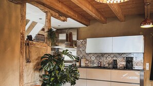 Ein gemütliches Wohnzimmer mit einer Ledersofa, einer großen Topfpflanze und einer Küche im Hintergrund.