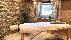 Ein Zimmer mit Steinwänden und Holzboden, ausgestattet mit einem Massagestuhl, einem Vorhangfenster und einem Blumentopf.