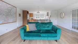 A modern living room with a teal sofa, a map on the wall, and a kitchen in the background.