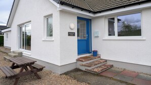 A white house with a blue door, a nameplate, and a picnic table outside.
