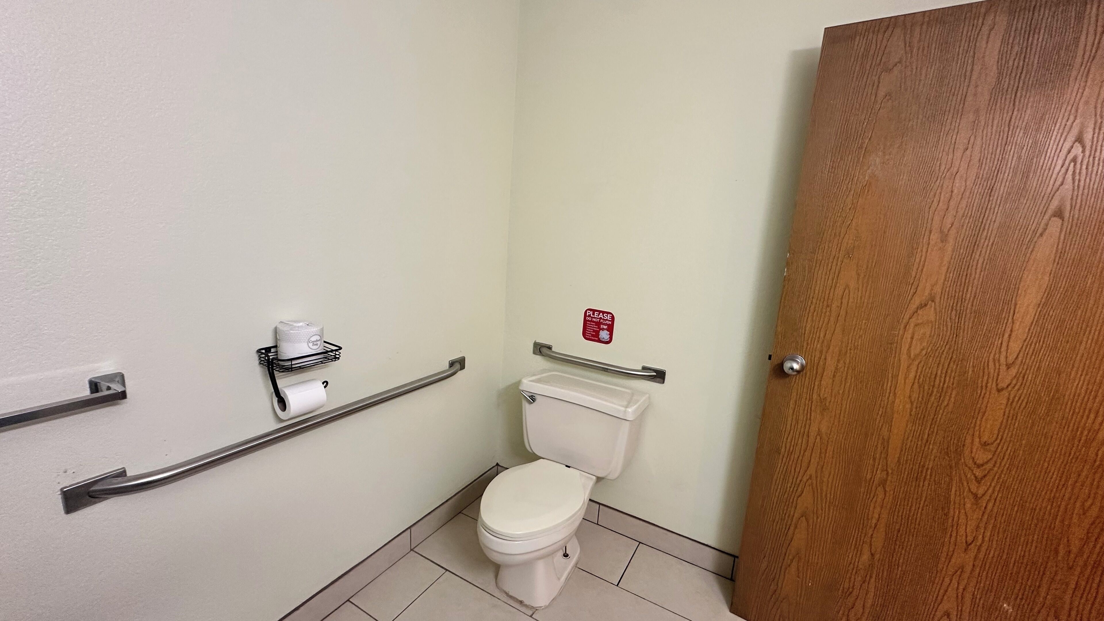 A small bathroom with a toilet, a handrail, a towel dispenser, and a door.