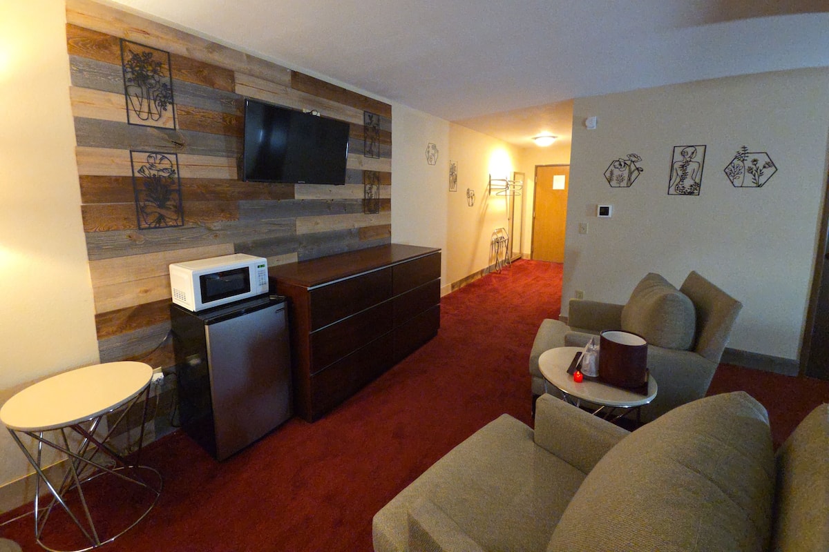 Ein kompakter Wohnraum mit Flachbildfernseher an einer Holzwand, einer kleinen Küchenzeile mit Mikrowelle, einer Couch und einem Couchtisch.