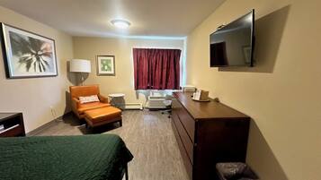 A hotel room with a bed, a desk, a chair, a TV, and a window with curtains.