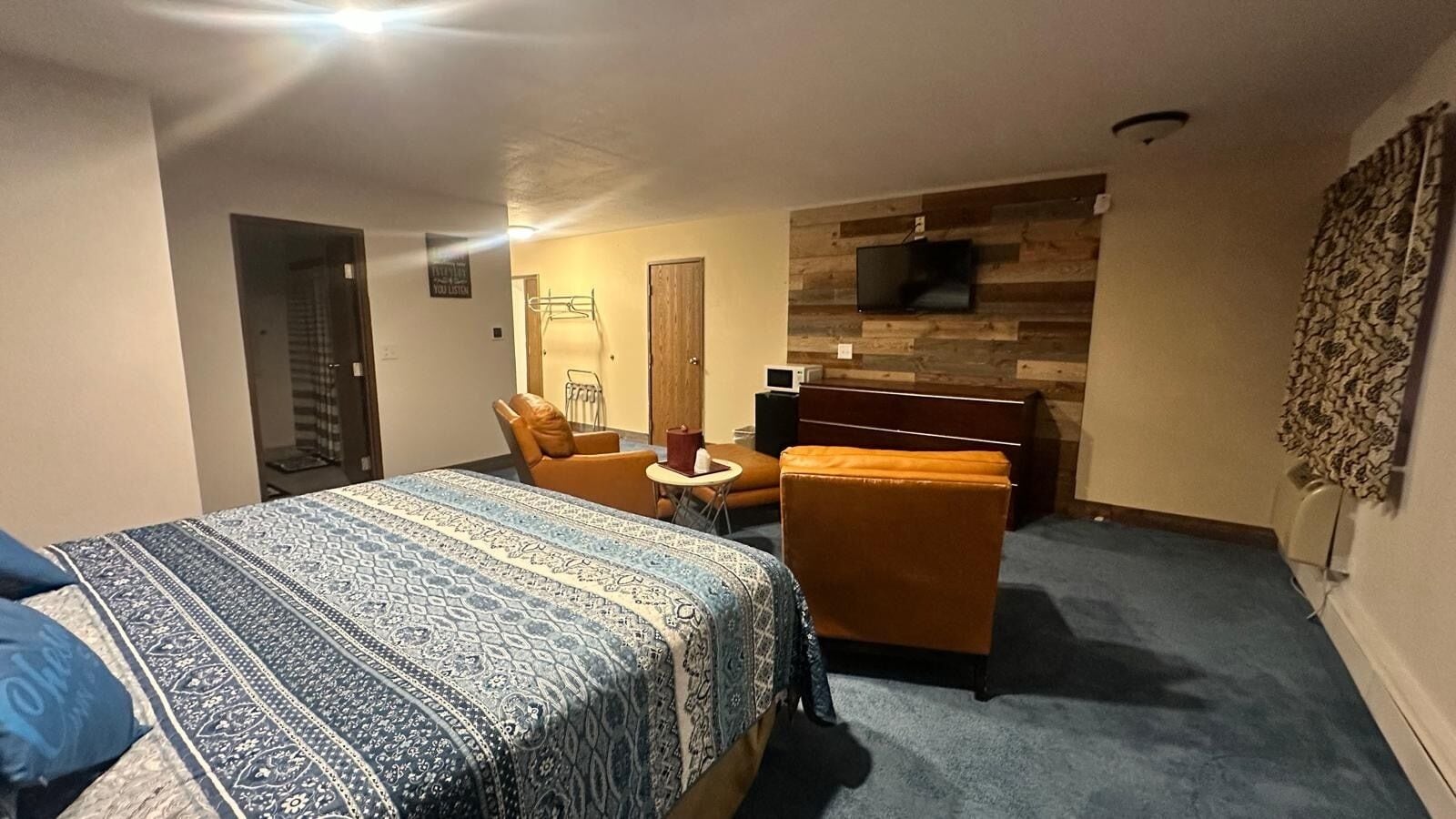 A hotel room with a bed, a chair, a small table, a TV, and a wooden accent wall.