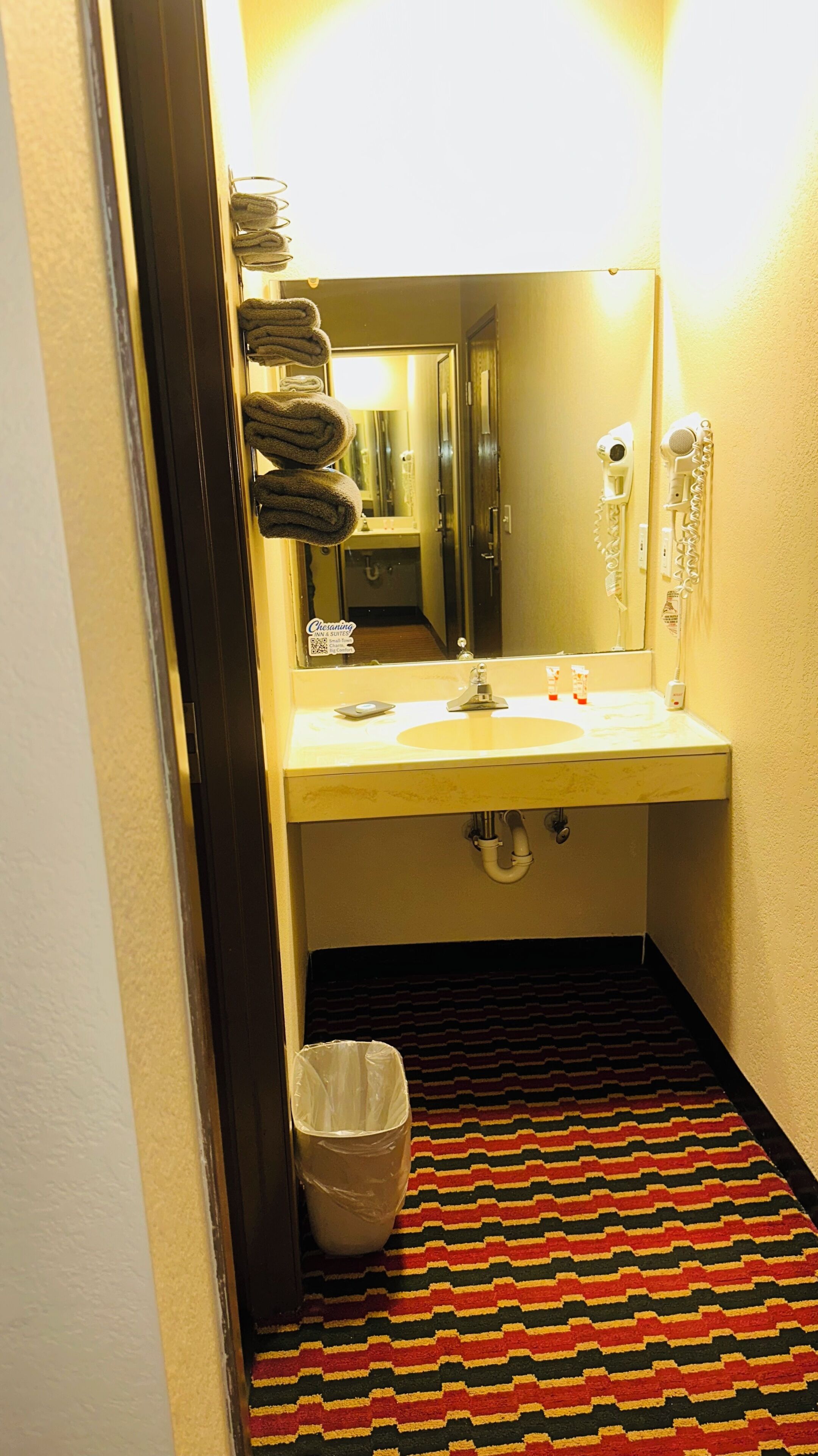 A hotel bathroom with a sink, mirror, towel rack, and a trash bin.