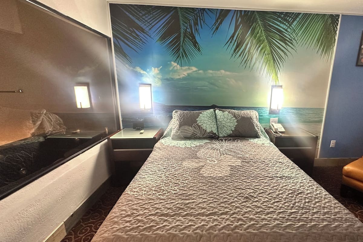 Ein Hotelzimmer mit einem Bett, einem Sessel, einem Nachttisch mit Telefon und einem Wandbild einer Strandlandschaft.