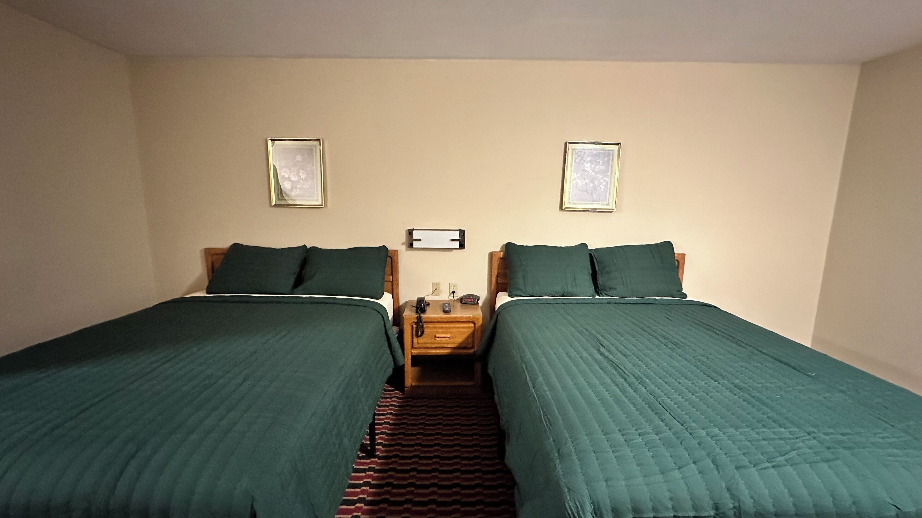 Habitación doble con dos camas, una mesita de noche y dos cuadros en la pared.