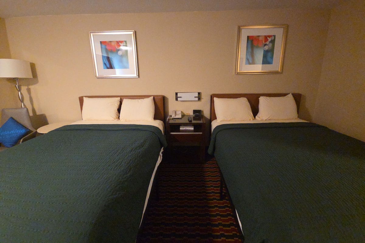 Ein Hotelzimmer mit zwei Betten, einem Nachttisch, einer Lampe und zwei gerahmten Bildern an der Wand.