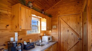 Cucina di una baita in legno con macchina da caffè, forno a microonde e lavandino.