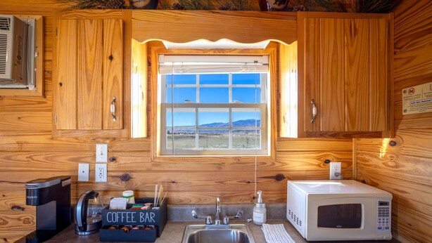 Cucina di una baita in legno con angolo caffè, lavello, forno a microonde e finestra con vista sulle montagne.
