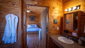 Interno di una baita in legno con bagno, dotato di lavandino, specchio e porta asciugamani.