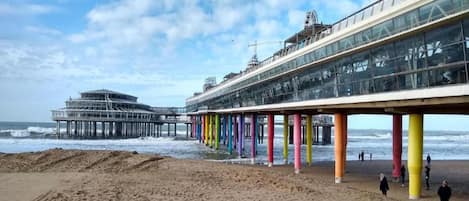 A pier with colorful supports and a glass structure extending over the beach.
