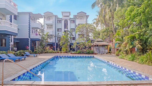 A swimming pool with tiled edges, surrounded by lounge chairs and potted plants, with multi-story buildings in the background. - Luxury Stays With Pool Near Calangute Beach (Calangute)