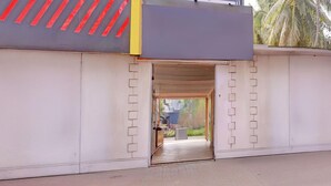 A building entrance with a clear pathway leading to a door, a visible outdoor area with plants, and a partial view of a building with a distinctive facade. - Luxury Stays With Pool Near Calangute Beach (Calangute)
