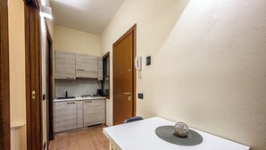 A compact kitchen with wooden cabinets, a white countertop, and a dining table with a decorative centerpiece. - Emilia Studios 2 (Modena)