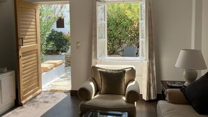 Ein Zimmer mit einem beigefarbenen Sessel, einer Couch, einem Fenster mit Vorhängen und einer Lampe auf einem Beistelltisch.