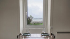 A dining table with four chairs, set with plates and wine glasses, facing a window with a view of the sea. - Gillean House-Spectacular beachfront property-Skye (Achnacloich)