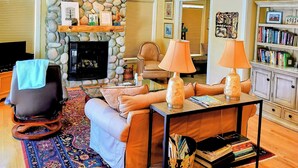 A cozy living room with a stone fireplace, comfortable seating, a coffee table, and a bookshelf. - Beautiful 2-bedroom townhome with Patio, WiFi, AC (Sisters)