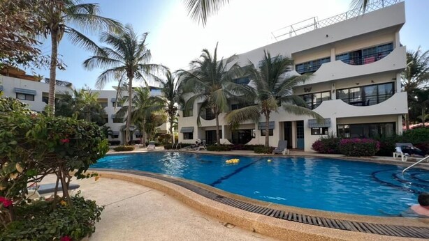 Una piscina rodeada de palmeras y un edificio de varios pisos con balcones.